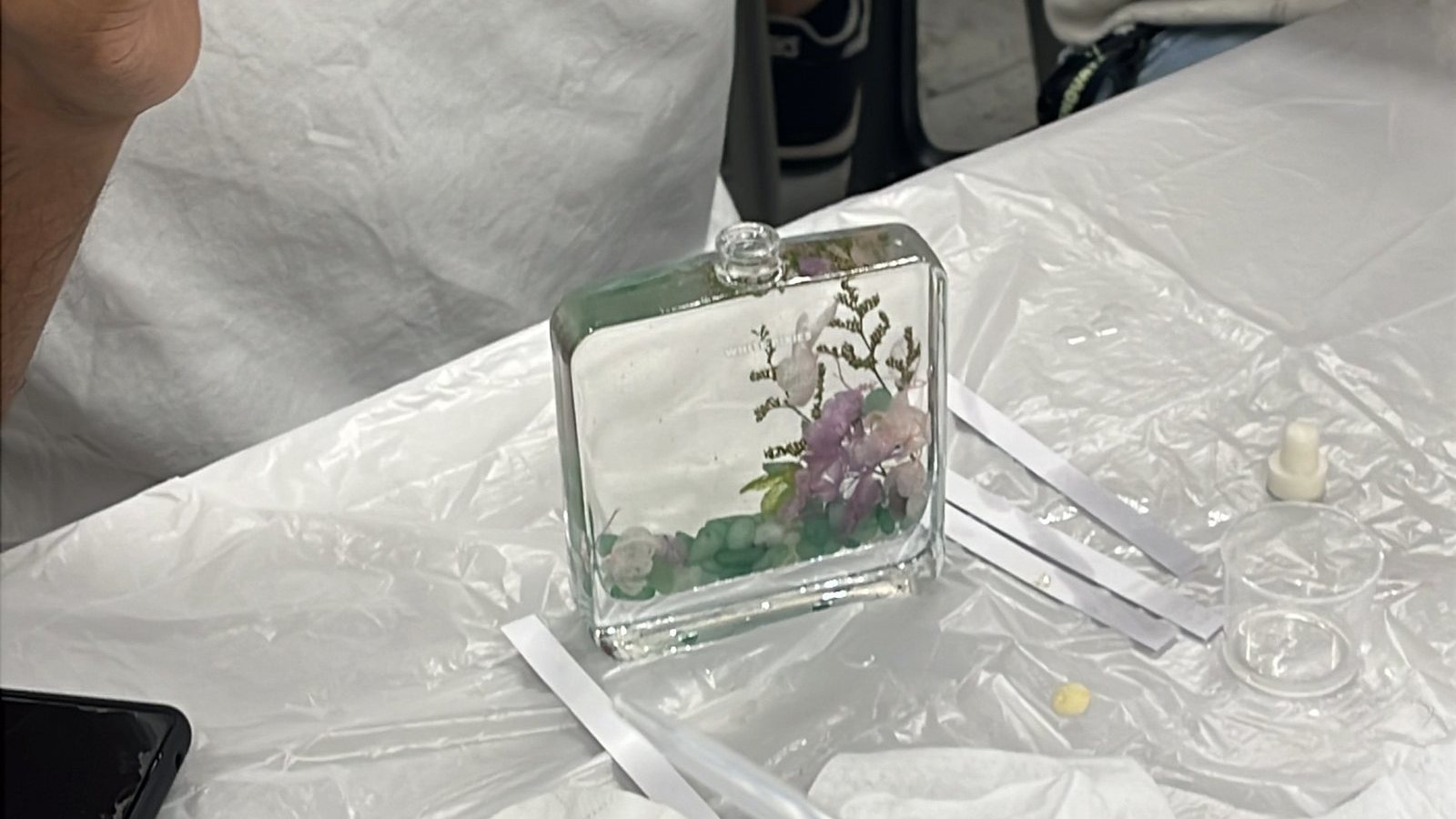 A glass reed diffuser bottle filled with dried flowers and greenery on a white table