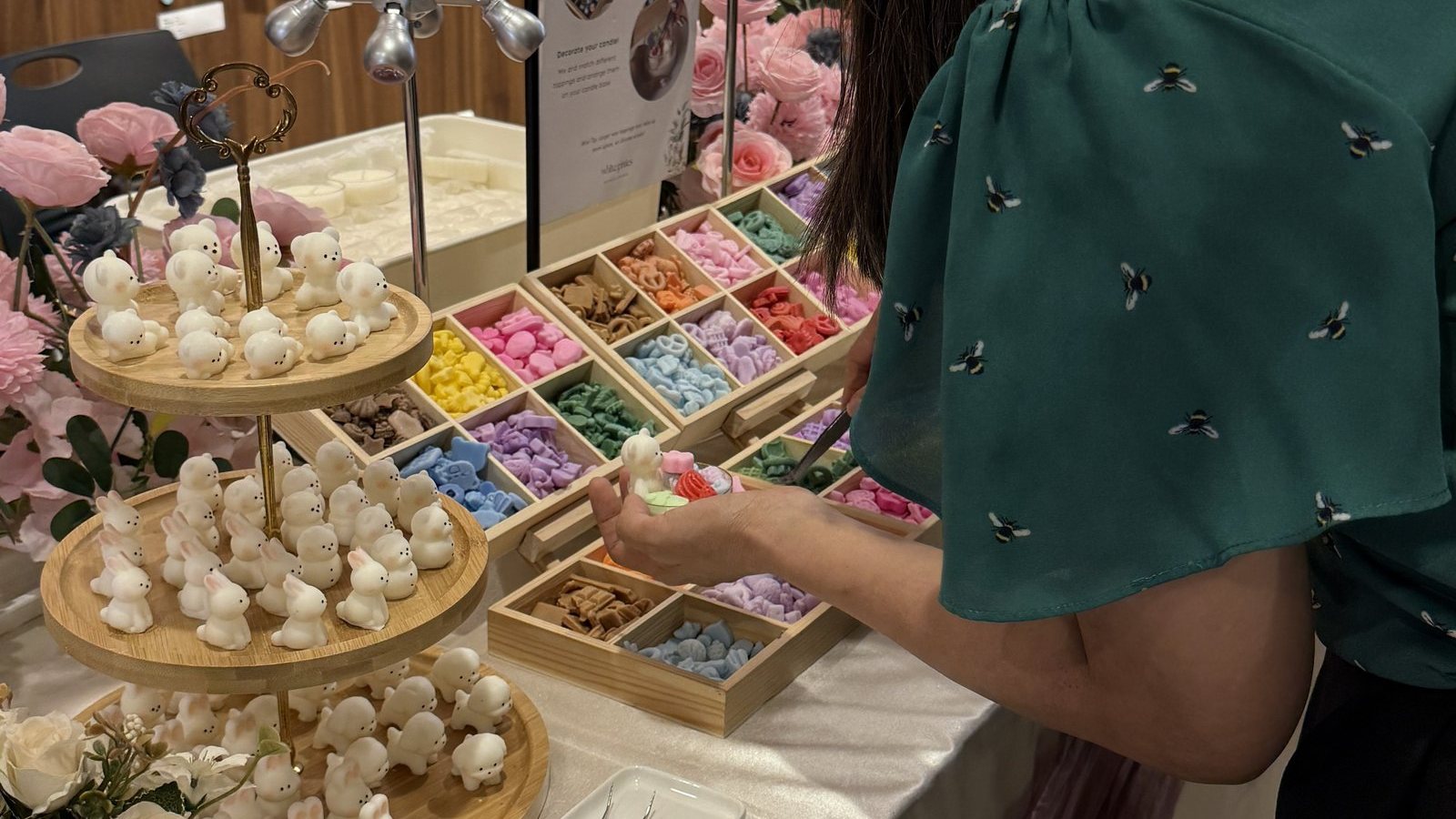 A guest picks wax toppings from trays at a candle decorating station dressed with pink flowers