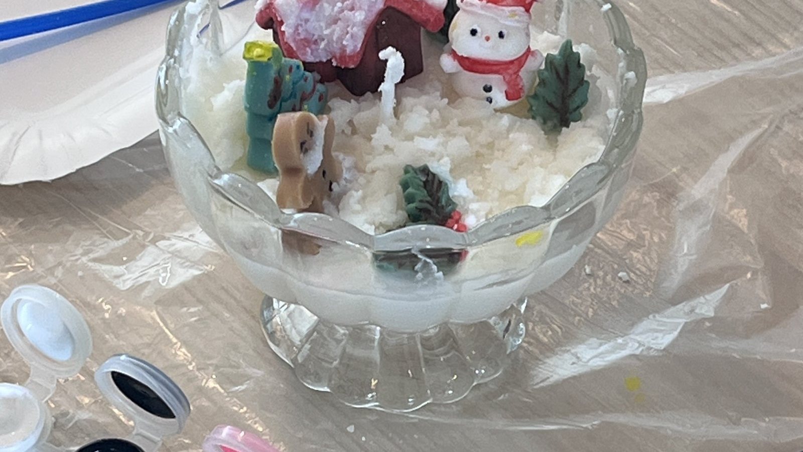 A candle in a glass dessert cup decorated with a small Santa, a snowman and a Christmas tree