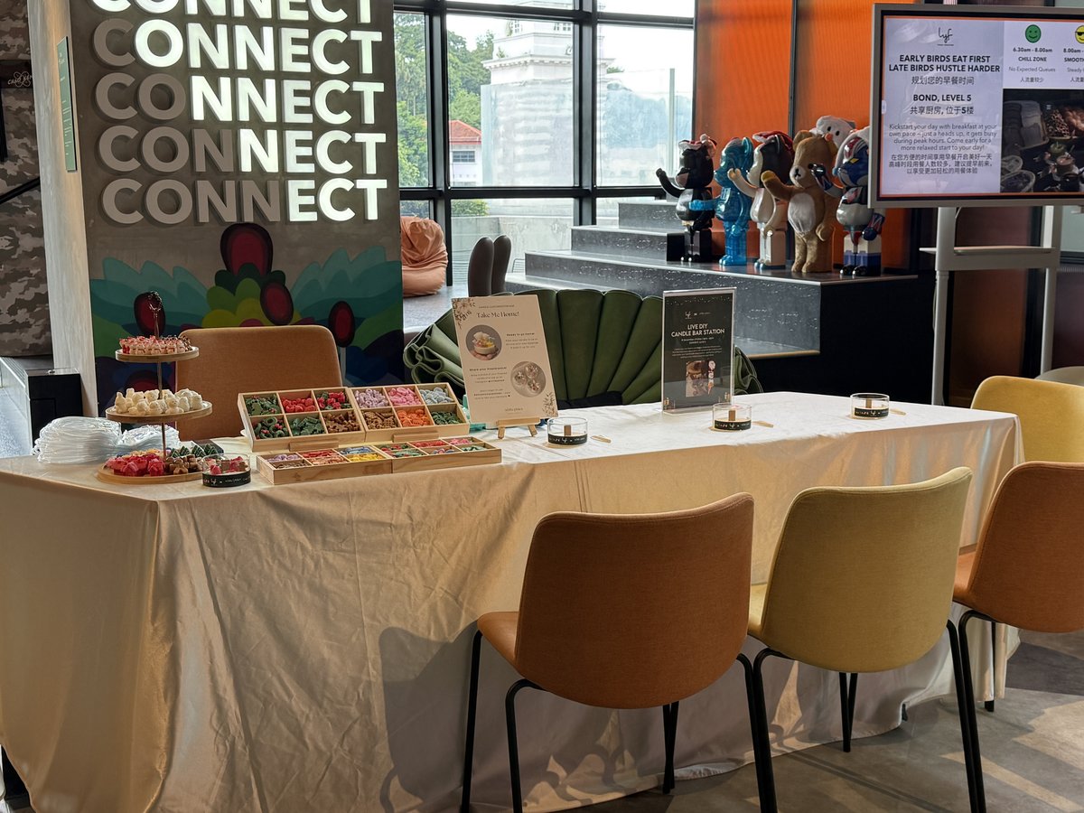 A live DIY candle bar station set up at a corporate event in Singapore, with trays of coloured wax toppings, tiered stands of wax decorations and labelled candle jars on a long table